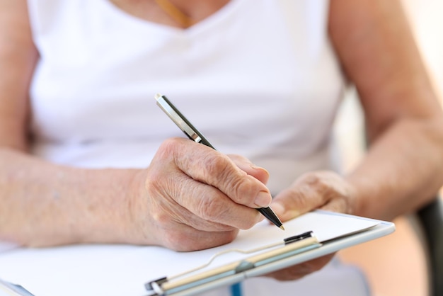 Gros plan sur les mains d'une vieille femme remplissant un formulaire en clinique ou en hospice soins de santé et médecine vieillesse