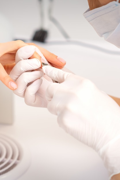 Gros plan sur un maître de manucure avec une pince à manucure coupe les cuticules des ongles féminins au salon de beauté.