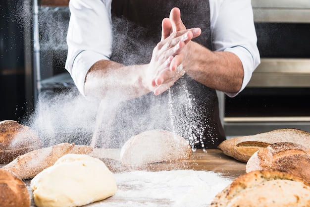 Gros plan, mâle, boulanger, main, épousseter, farine, bureau, bois, pain cuit