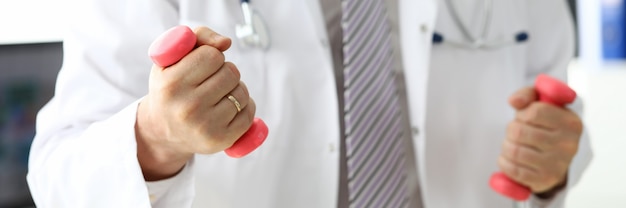 Gros plan, mâle, mains, tenue, haltères Médecin en blouse médicale montrant des exercices avec des haltères roses au patient. Mode de vie sain et concept de médecine