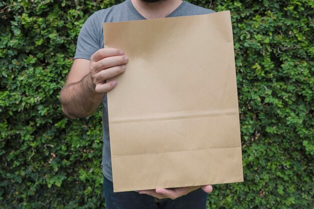 Gros plan mâle tient dans la main un sac en papier kraft blanc vide clair marron pour emporter ou livraison