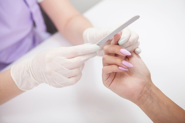 Gros plan d'une manucure à l'aide d'un lime à ongles, travaillant avec une cliente