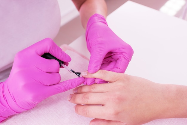 Gros plan de manucure professionnelle. Vernis gel nude sur les ongles. Le maître féminin dans le salon fait une procédure de spa pour les mains du client. Industrie de la beauté, concept de détente.