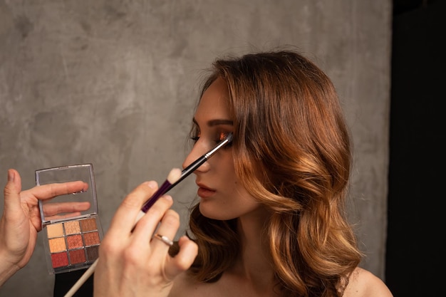Gros plan d'une maquilleuse faisant le maquillage des yeux pour un modèle de fille sur fond gris en studio. Maquillage professionnel. Place pour le texte