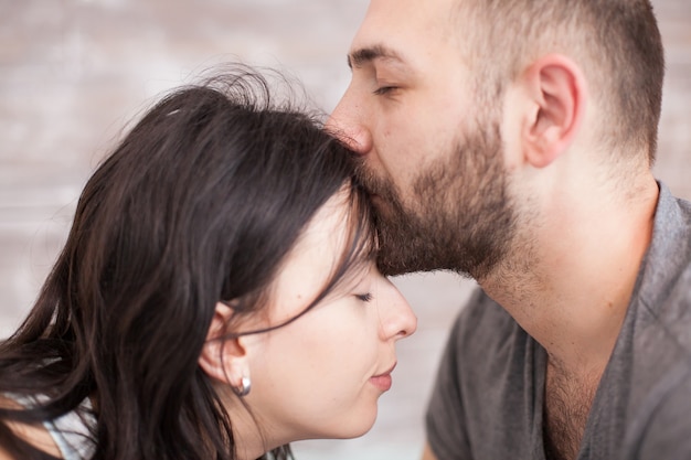 Gros plan sur un mari barbu embrassant le front de sa femme le matin.