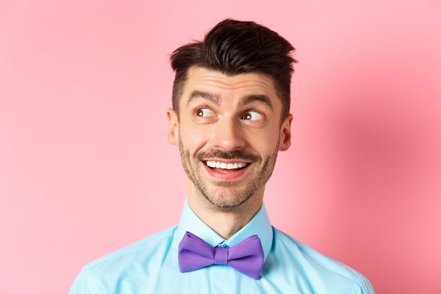 Gros plan d'un mec souriant amusé avec moustache, pointant et regardant à gauche heureux, regardent le logo, debout sur le rose.