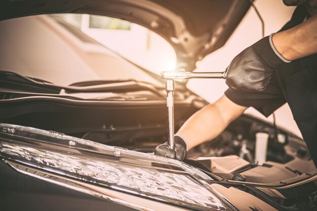 Photo gros plan mécanicien automobile à main utilisant la clé pour réparer le problème du moteur de voiture concepts de contrôle et d'inspection entretien et entretien de la voiture