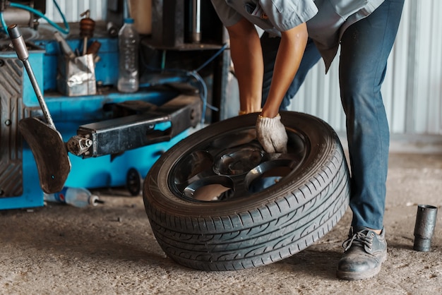Gros plan Le mécanicien automobile remplace le pneu sur la roue dans l'atelier de réparation automobile.