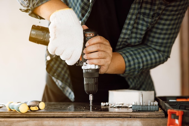 Gros plan d'un mécanicien masculin tenant une perceuse-visseuse électrique sans fil avec une vis à bois dans l'usine Travailler avec la vis Charpentier professionnel Concept de meubles à la maison