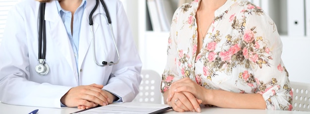 Gros plan sur un médecin et un patient assis à la table, juste les mains.