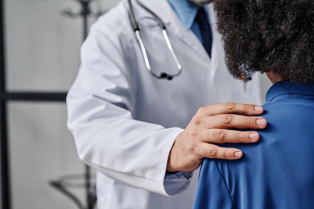 Gros plan sur un médecin tenant l'épaule d'une patiente et la soutenant dans sa maladie difficile