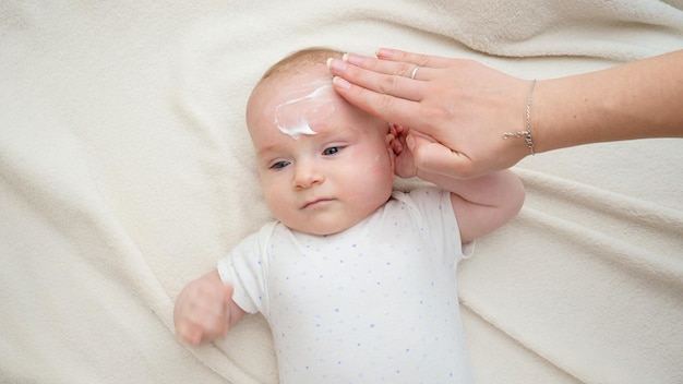 Photo gros plan de la mère appliquant une crème hydratante sur la peau du visage de son petit bébé concept de nouveau-né