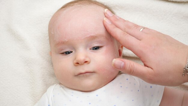 Photo gros plan de la mère appliquant de la crème pour hydrater et nettoyer le visage de son bébé concept de nouveau-né