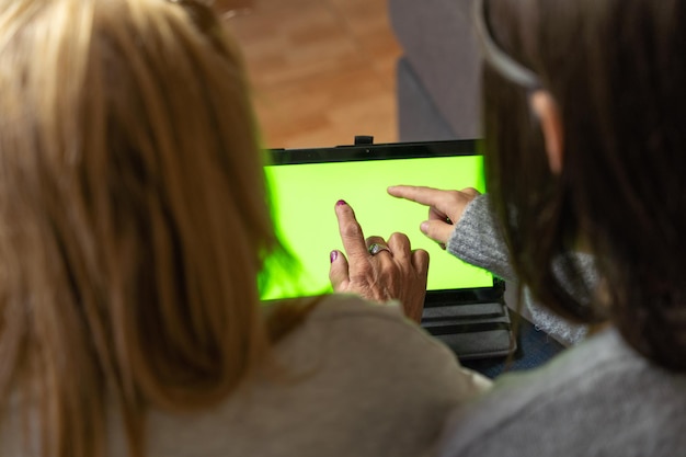 Gros plan de la mère et de la fille avec des dos méconnaissables l'un à l'autre en utilisant la tablette sur le canapé assis sur le canapé