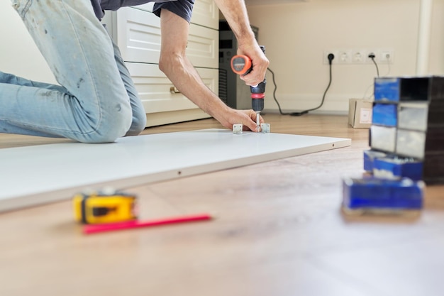 Gros plan sur les meubles et les mains du menuisier avec outil professionnel, tournevis à la main, assemblage de meubles à la maison. Rénovation, nouveau mobilier, travail procédé de menuiserie