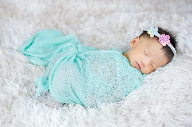 Gros plan mignon nouveau-né portant un bandeau de fleurs sur des tapis de laine, concept de mode
