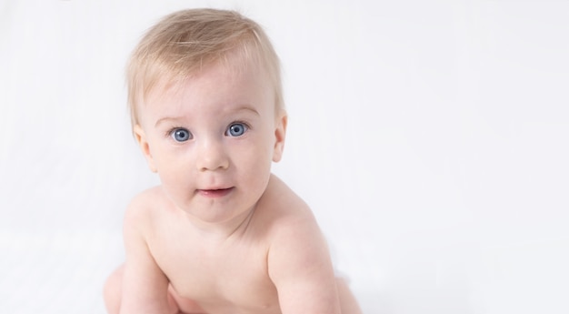 Gros plan mignon petit adorable drôle étonné caucasien blond topless bébé fille ou garçon sur fond blanc, gris clair, regardant la caméra. Peau saine. Soins de bébé, concept d'enfance heureuse. Espace de copie pour le texte.