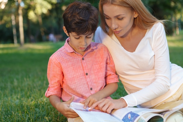 Gros plan d'un mignon petit garçon et son enseignante lisant un livre à l'extérieur, copiez l'espace