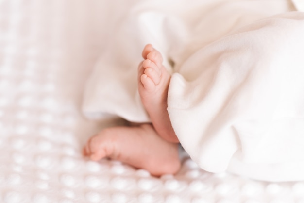 Gros plan de minuscules adorables pieds de bébé rose nu pendant que l'enfant dort sur une couverture blanche