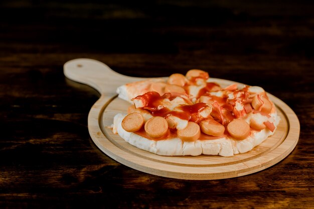 Gros plan de la mise au point sélective de la pizza sur un plateau en bois sur la table en bois sombre.