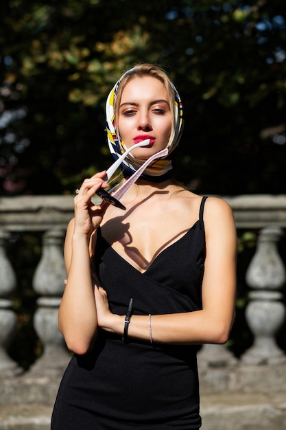 Gros plan d'un modèle glamour avec des lèvres rouges portant un châle et une robe noire posant avec la lumière du soleil