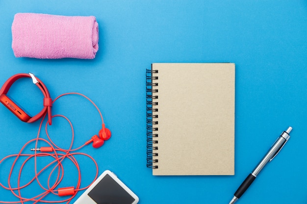 Gros Plan De La Montre Rouge Et Des écouteurs Rouges Avec Accessoires Sur Fond De Papier Bleu, Concept De Fond De Remise En Forme.