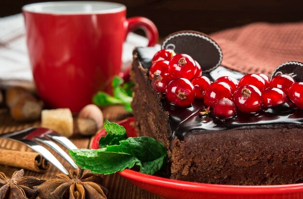 Gros plan d'un morceau de gâteau au chocolat décoré de groseilles rouges sur le fond d'une tasse rouge