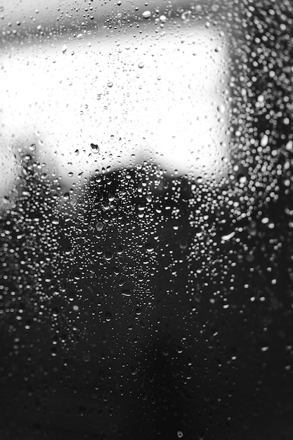 Gros plan des motifs de condensation sur la vitre, gouttelettes d'eau avec réflexion et réfraction de la lumière, arrière-plan abstrait noir et blanc.