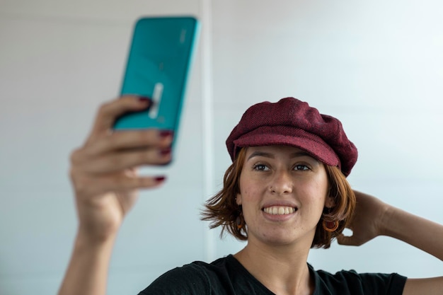Gros plan moyen d'une jeune femme latino-américaine de 22 ans avec une casquette et des cheveux rouges prenant un autoportrait avec son téléphone portable Concept de technologie