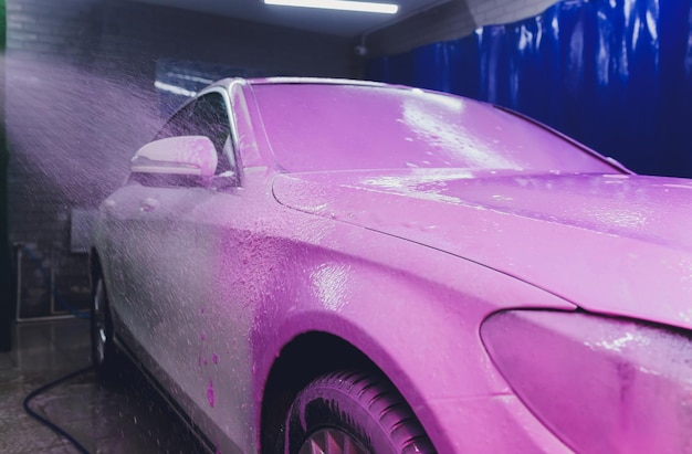 Gros plan sur le nettoyage de la voiture à l'aide d'eau à haute pression Nettoyeur à jet haute pression en cours de lavage de voiture en mousse de couleur rose