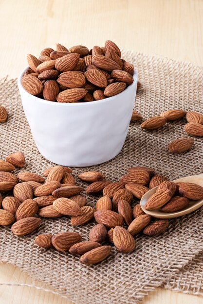 Gros plan des noix d'amandes sont versés dans un bol blanc sur une table en bois.