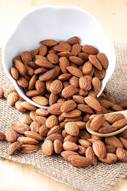 Gros plan des noix d'amandes sont versés dans un bol blanc sur une table en bois.