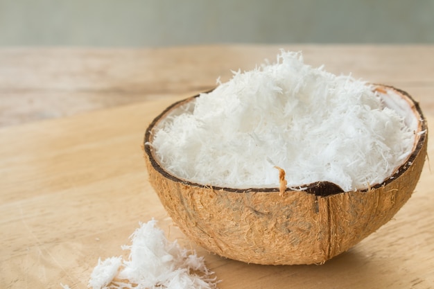 Gros plan de noix de coco fraîchement râpée en coque sur table en bois.