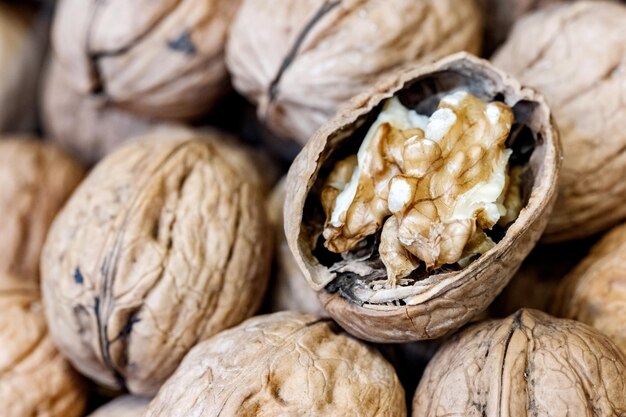 Gros plan sur une noix crue fendue sur un tas de noix entières avec des coquilles