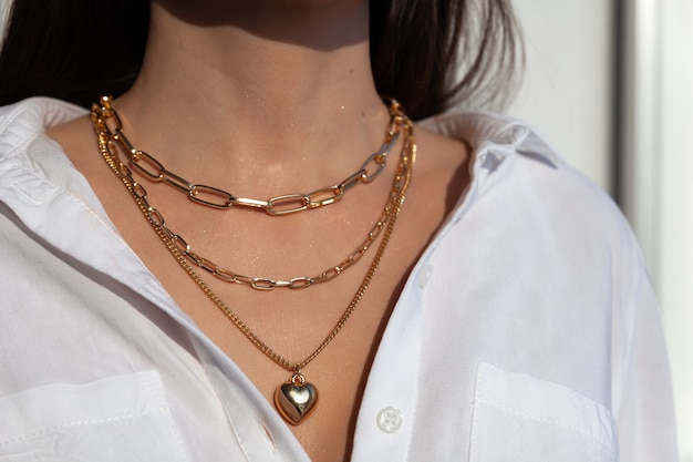 Gros plan de nombreuses chaînes en or élégantes avec pendentif en forme de coeur sur le modèle en chemise blanche, collier en métal