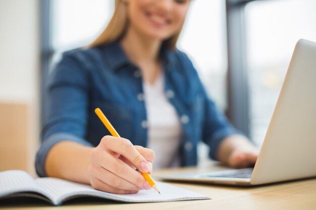 Gros plan des notes prises par une femme gaie agréable et intelligente tout en travaillant au bureau