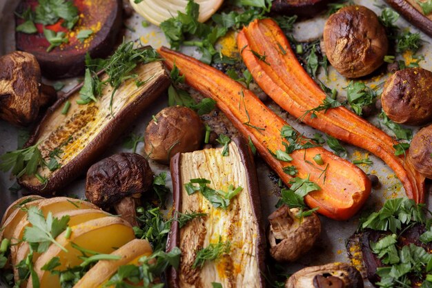 Gros plan sur la nourriture végétarienne Tranches cuites au four d'aubergines betteraves carottes oignons pommes de terre champignons entiers épices et herbes sur papier parchemin