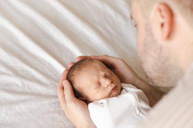 Gros plan d'un nouveau-né mignon brun poilu caucasien dormant Un enfant de deux semaines sur le lit dans des mains masculines Homme méconnaissable père tenant un enfant Carelovehappiness concept