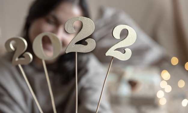 Photo gros plan des numéros en bois 2022 sur des bâtons dans des mains féminines sur fond flou avec bokeh.