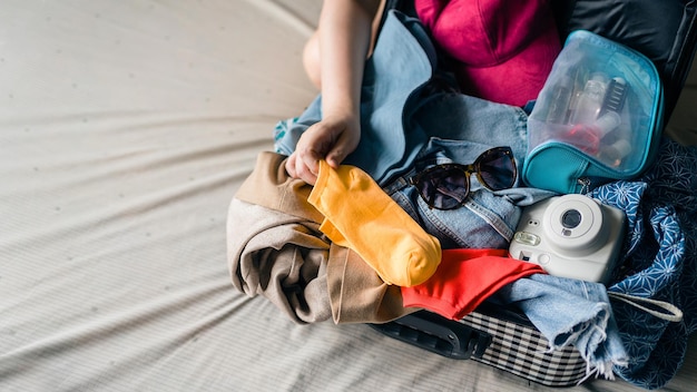 Gros plan sur des objets en désordre tels que des lunettes de soleil, un sac cosmétique pour appareil photo polaroid et un petit sac, essayez de tout mettre dans les bagages avec un emballage en difficulté pour partir en vacances