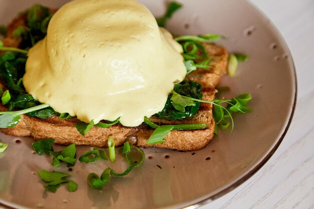 Gros plan d'œufs alternatifs végétaliens plat bénédictine avec du pain complet sauce hollandaise crémeuse à base de plantes tofu jeunes oignons verts pousses de pois