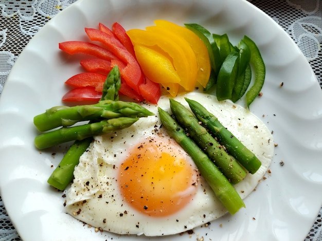 Gros plan des œufs au plat avec des légumes comme une tranche de poivron doux aux asperges sur une plaque blanche