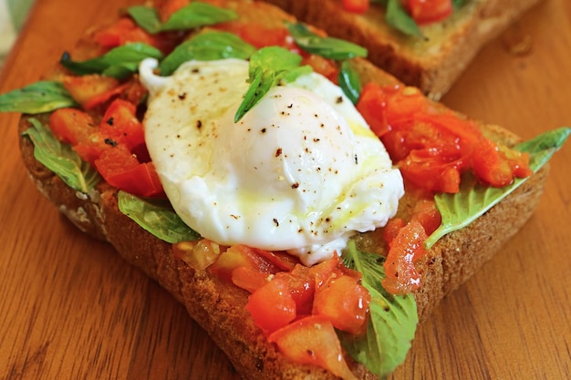 Gros plan d'œufs pochés appétissants sur du pain grillé au basilic frais et à la tomate