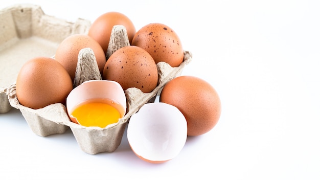 Gros plan des œufs de poule crus dans une boîte à œufs et une coquille isolée