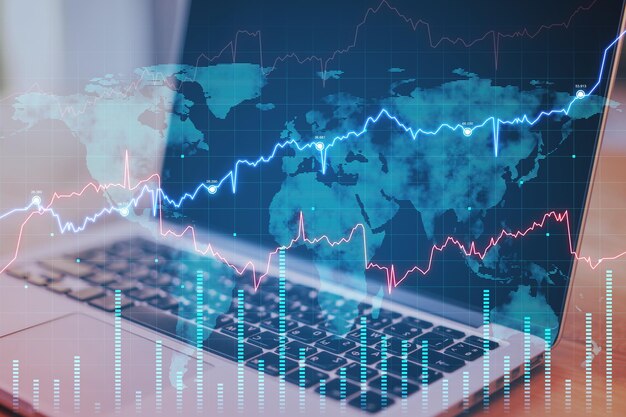 Gros plan d'un ordinateur portable sur le bureau avec un graphique forex abstrait et une carte Concept de commerce et d'échange de données Fintech Double exposition