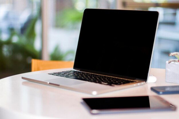 Photo gros plan d'un ordinateur portable moderne avec écran blanc sur une table blanche dans une maquette intérieure ensoleillée concept d'entreprise et de technologie