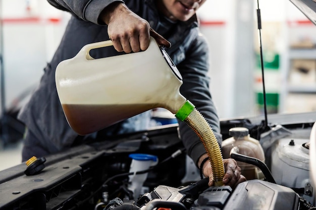 Gros plan d'un ouvrier d'atelier de mécanicien automobile versant de l'huile dans le moteur du garage