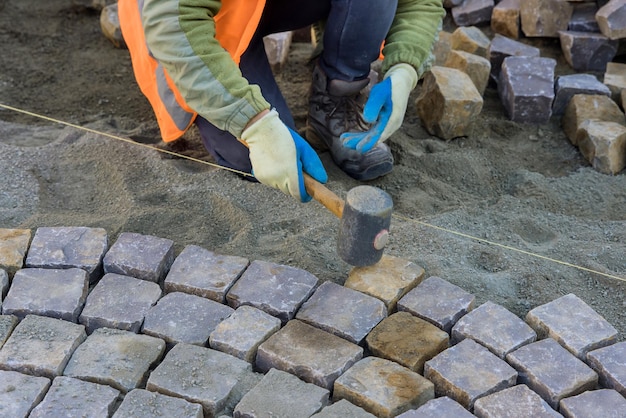 Gros plan sur un ouvrier du bâtiment installant des pierres de chaussée sur un trottoir près de la route