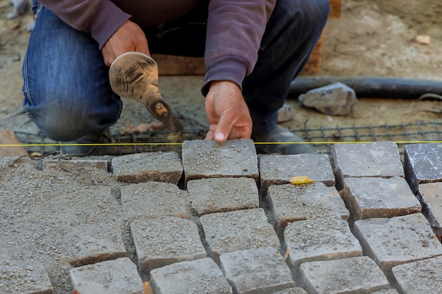Gros plan sur un ouvrier du bâtiment installant et posant des pierres sur le trottoir de la route