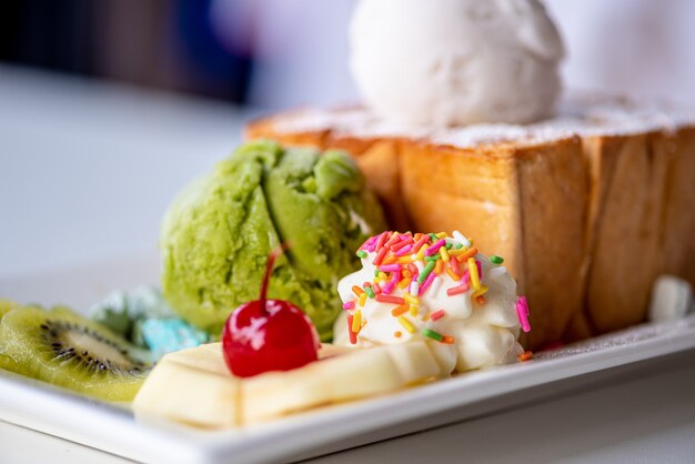 Photo gros plan de pain grillé au miel servi avec une boule de crème glacée au thé vert et au lait de coco, décorer avec des cerises, des pommes, des kiwis et du sucre à la crème saupoudrer sur un plat blanc, une collation douce et fraîche en été